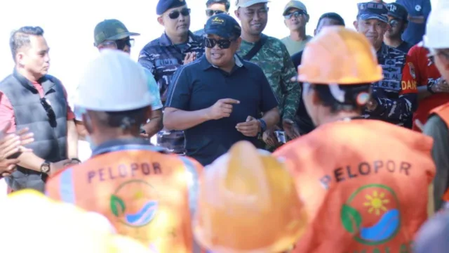 Bupati Takalar Firdaus Dg Manye mengenakan kaos hitam, topi hitam, dan kacamata hitam sedang berdiskusi dengan para pekerja berhelm proyek orange bertuliskan Pelopor di Pulau Sanrobengi, didampingi jajaran TNI AL dan dinas pariwisata
